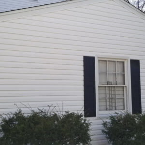 Photo of a house's side with a window and white vinyl siding that was recently restored via power washing