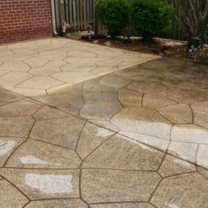 Photo of concrete patio with four sections and one section being fully cleaned by power washing